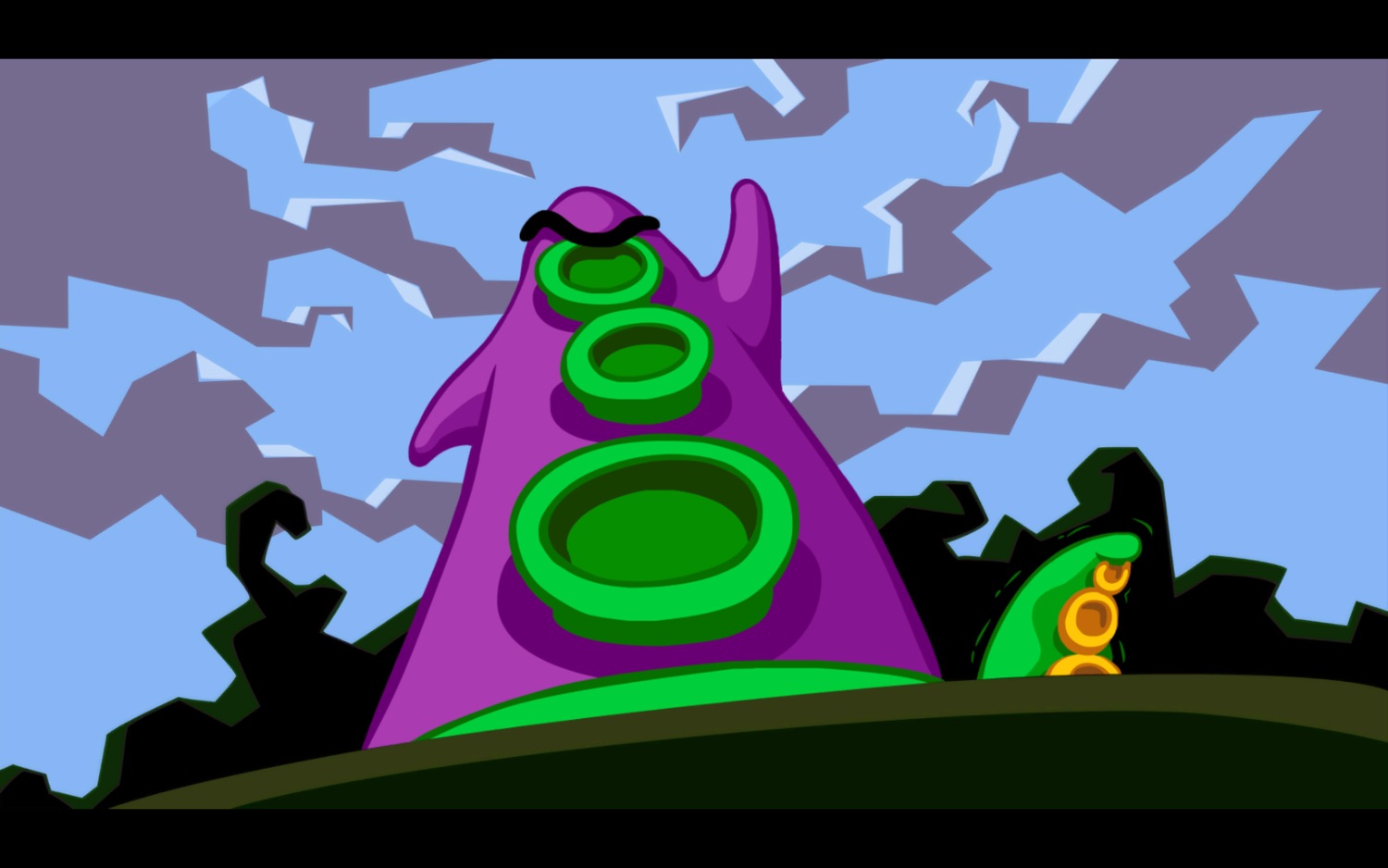 Screenshot from Day of the Tentacle showing Purple Tentacle getting his hands. It’s a worm’s eye view and we’re looking up at him as he threatens to take over the world. In the background, Green Tentacle is quivering.